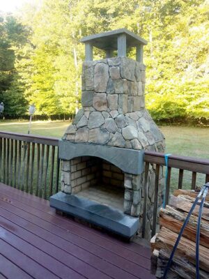 Outdoor fireplace connected to a dec with a stone fireplace cap