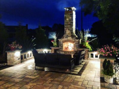 outdoor fireplace with brick accents at night with a fire burning